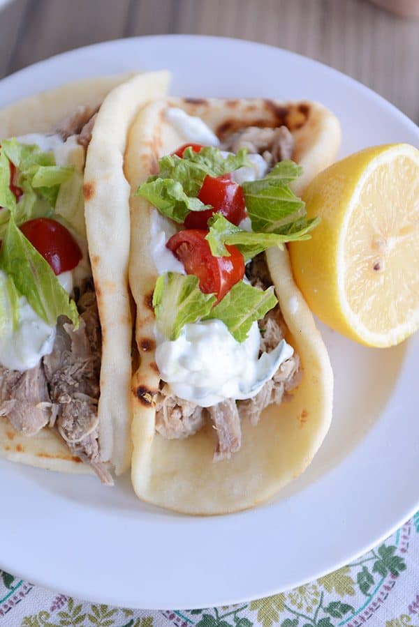 Top view of a Greek pork taco on flatbread with a half lemon next to it. 