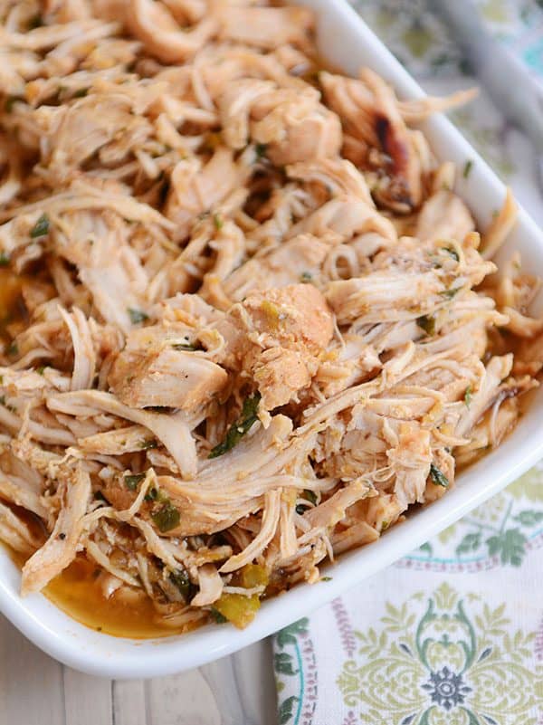 A white dish full of cooked, shredded chicken with bits of cilantro in it.