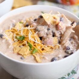 Instant Pot white chicken chili in white bowl with spoon and shredded cheese.
