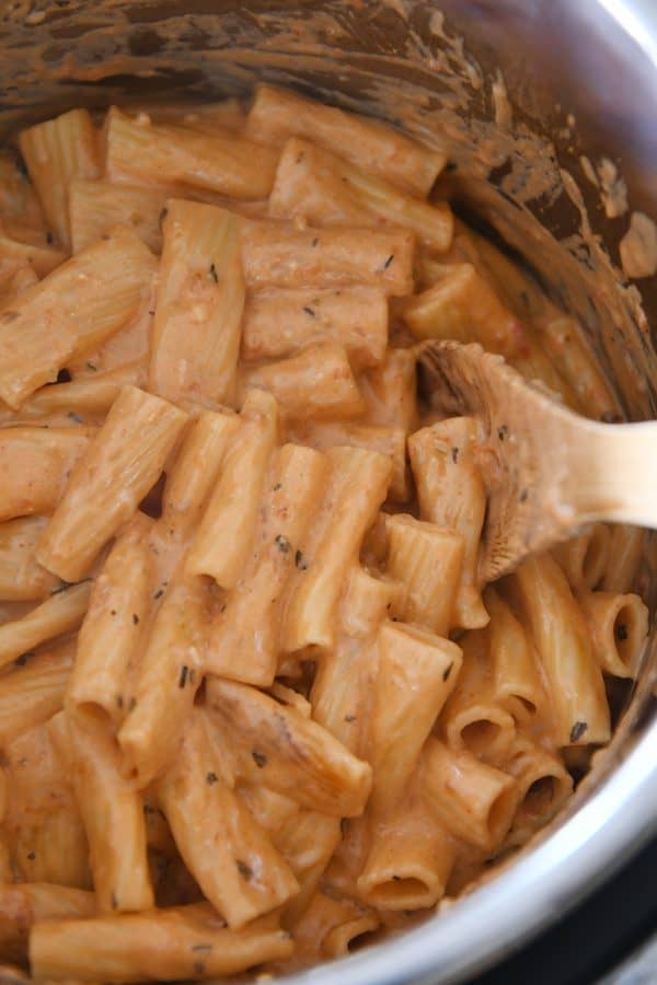 Stirring Instant Pot creamy baked ziti with metal spoon.