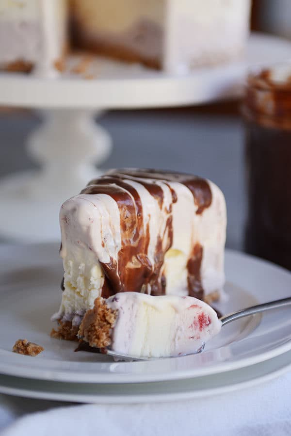 A slice of ice cream cake with a bite taken out on a white plate.