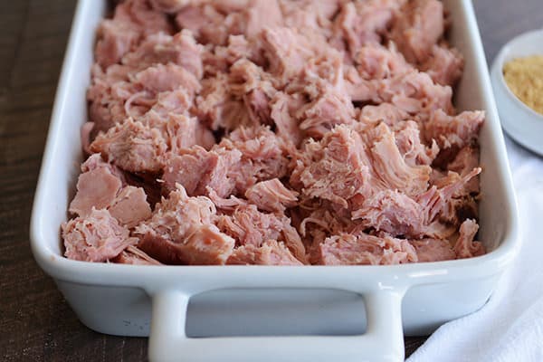 A white dish full of shredded, baked ham. 