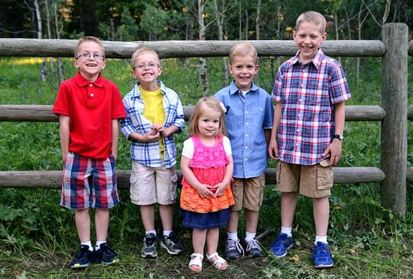 five little kids standing against a wooden fence outside