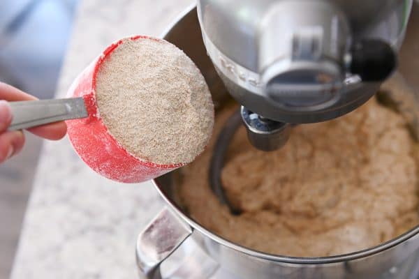 Whole wheat flour getting poured into a metal KitchenAid bowl.