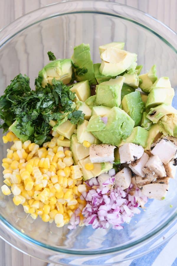 Avocado chicken salad ingredients - cilantro, avocado, corn, onion, chicken - in glass bowl.