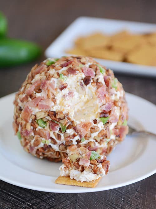 A bacon jalapeno cheeseball with a bite taken out on a cracker. 