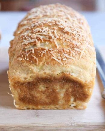 Loaf of parmesan bagel bread on wood cutting board.