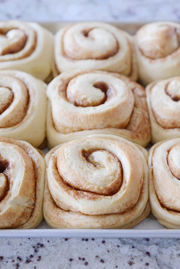 A sheet pan of cooked, unfrosted cinnamon rolls. 
