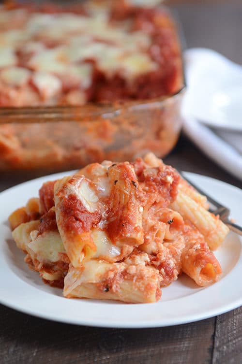 Scoop of baked ziti pasta with melted cheese and red sauce on a white plate.