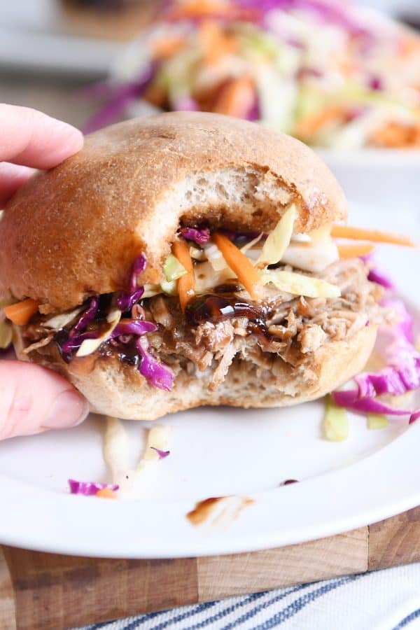 Bite taken out of honey balsamic BBQ pork sandwich on white plate.