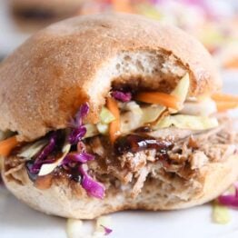 Bite taken out of honey balsamic BBQ pork sandwich on white plate.