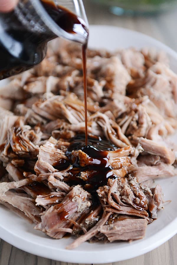 A full plate of shredded pork with a balsamic glaze getting poured over the top.