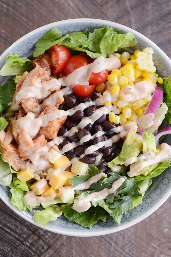 Top view of a BBQ chicken, black bean, and vegetable salad drizzled with dressing.