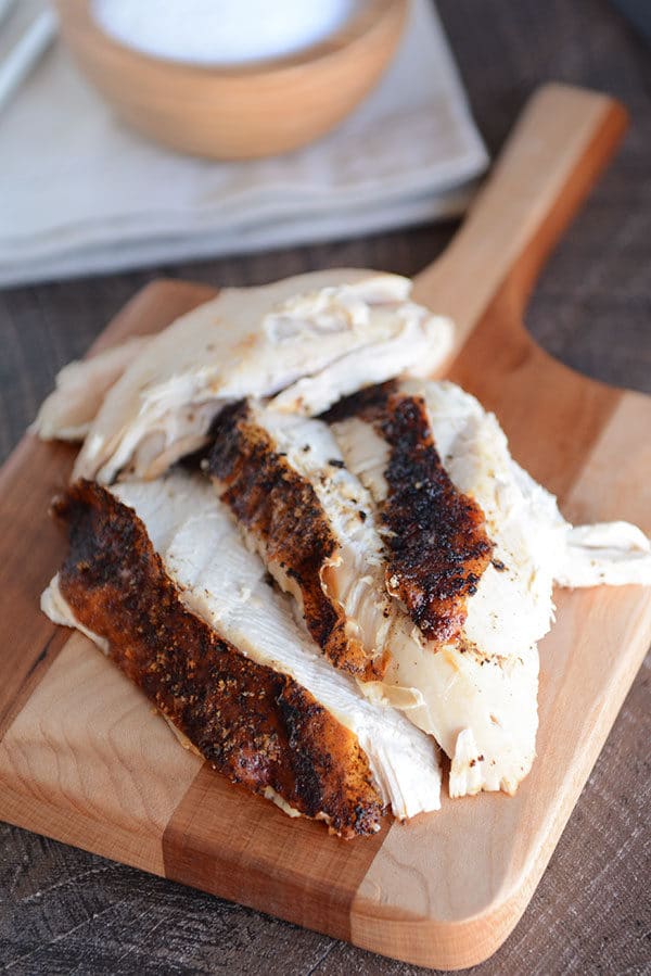 A small wooden cutting board with thick slices of roast chicken on top.
