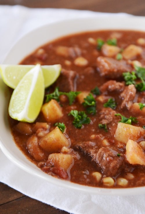 A white bowl of beef and sweet potato stew with lime wedges on the side.