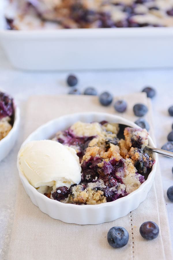 A white ramekin full of blueberry dump cake and a scoop of vanilla ice cream. 