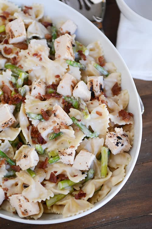 A white oval bowl full of creamy bowtie pasta with cubed chicken and asparagus.