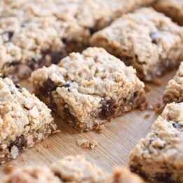 Slab of monster cookie bars cut into squares on wood board.