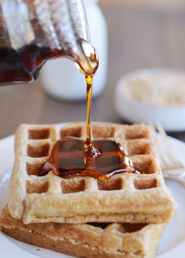 Syrup being poured over two thick Belgian waffles.