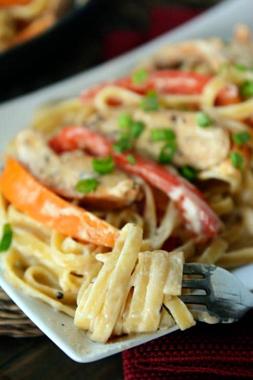 A fork with creamy fettucine wrapped around it from a platter of chicken cajun pasta.