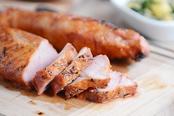 A grilled pork tenderloin with thick slices cut off on a wooden cutting board.