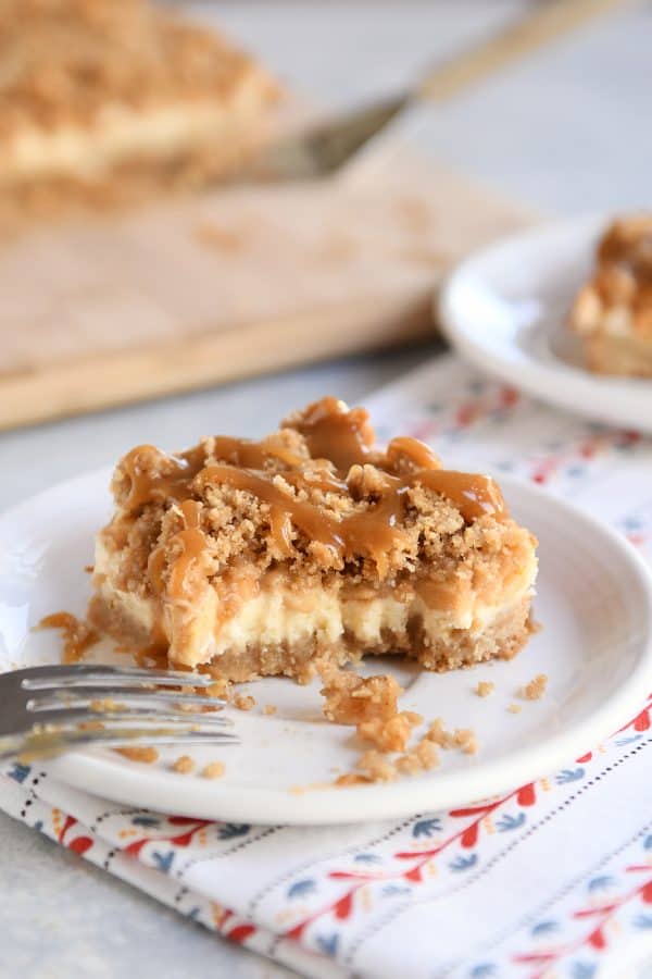 Half eaten caramel apple cheesecake bar on white plate.
