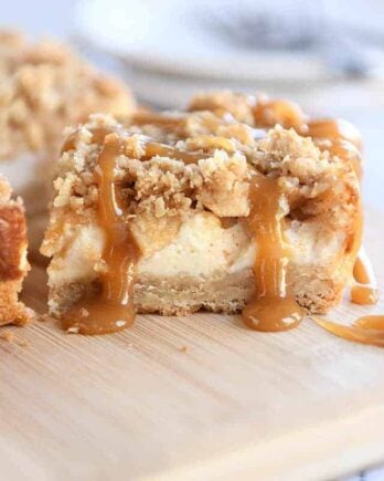 Caramel apple cheesecake bar drizzled with caramel on wood cutting board.