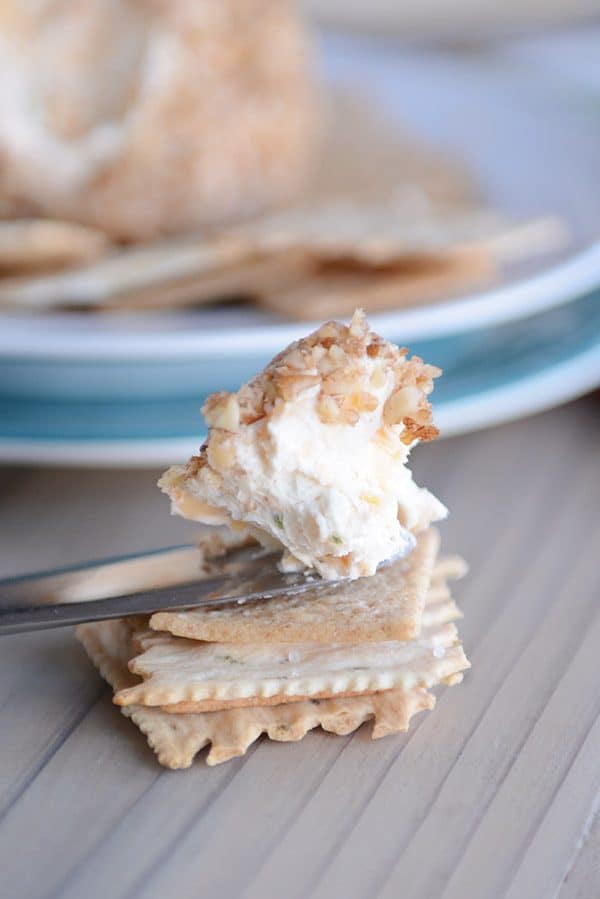 Piece of cheeseball on a knife above a stack of crackers.
