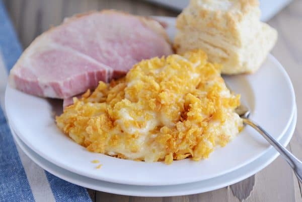 Scoop of cheesy funeral potatoes on plate with ham and biscuit