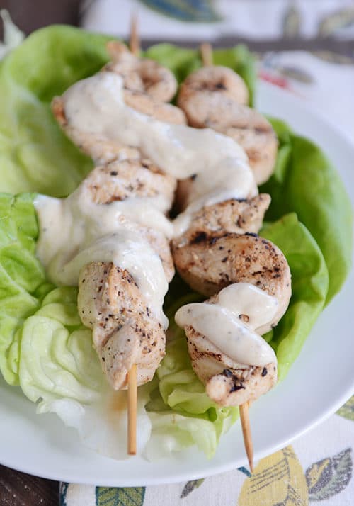 Two grilled chicken skewers drizzled with a yogurt hummus sauce. 
