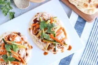 Top down view of Chicken banh mi flatbread with pickled cucumbers and carrots on white platter.