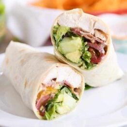 Chicken BLT burritos cut in half on white plate.
