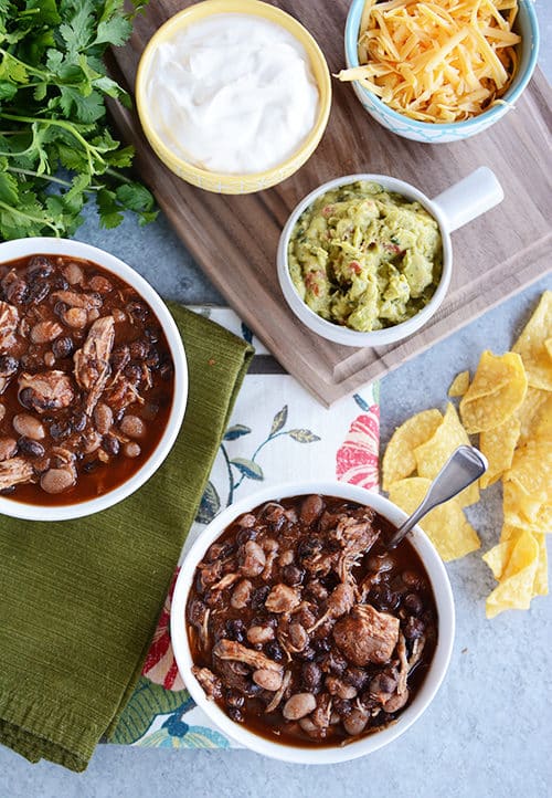 Top view of bowls of black bean chicken chili, cheese, sour cream, and guacamole.