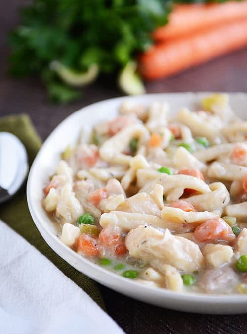 A white bowl full of thick chicken noodle stew.