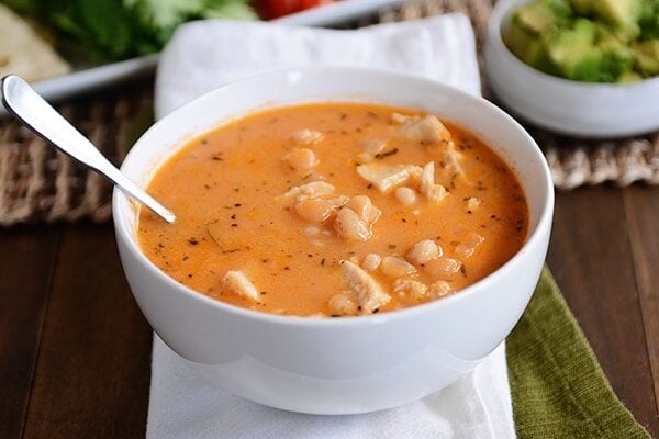 A white bowl full of white bean chicken chili with a spoon in it.
