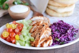 White platter with grilled chicken shawarma, cucumbers, tomatoes and cabbage slaw.