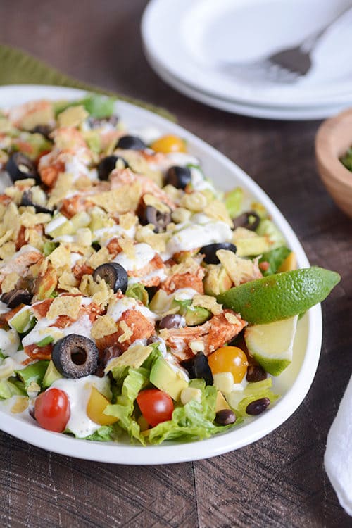 A large bowl with a chicken taco salad loaded with toppings and drizzled with dressing.