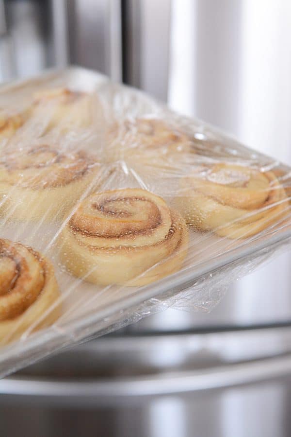 A pan of cinnamon rolls rising with saran wrap covering them. 