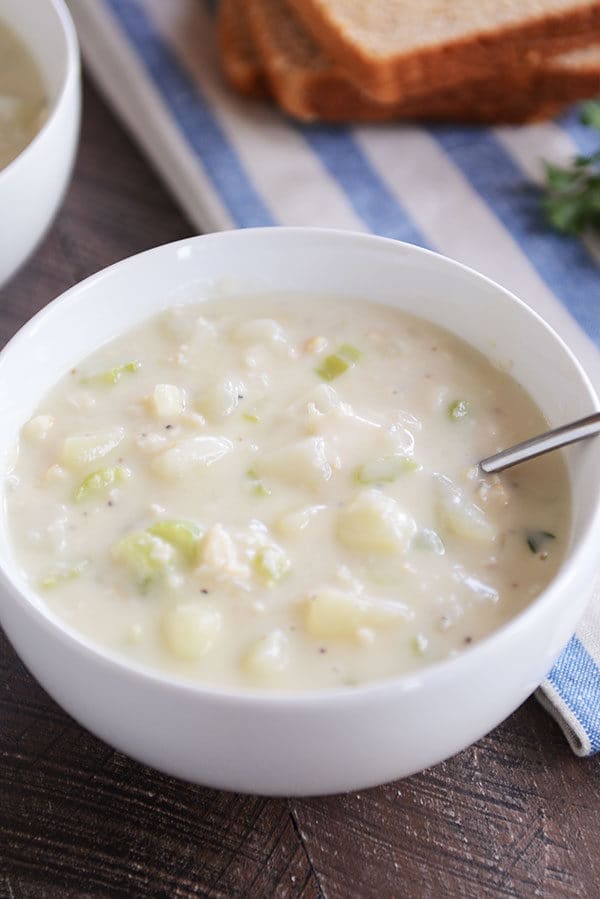 A white bowl of clam chowder with a spoon it it.