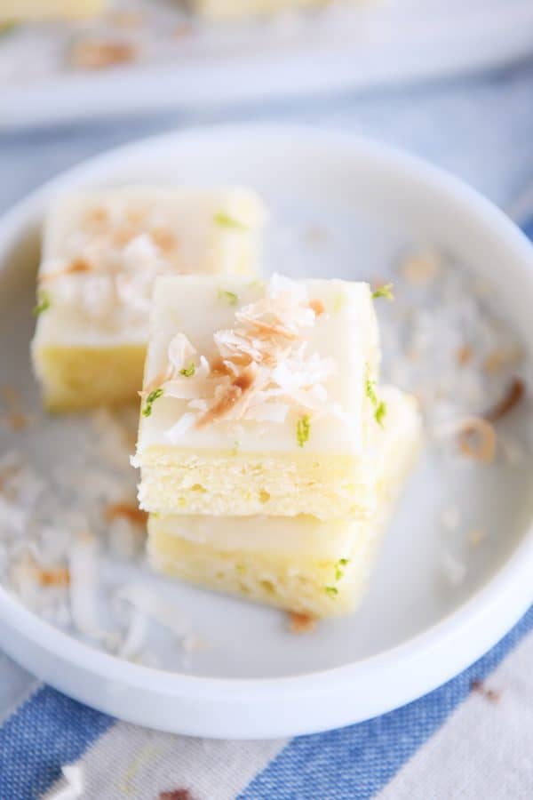 Toasted coconut lime bars stacked on white circle plate.