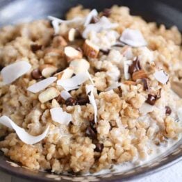 Coconut milk steel cut oats in brown bowl with chocolate chips, almonds and coconut.