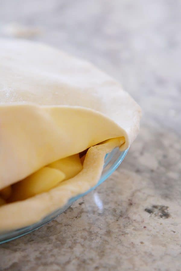 An apple pie with the top crust getting laid on.