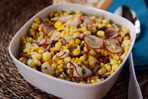 A white bowl full of fresh corn and radish salad. 