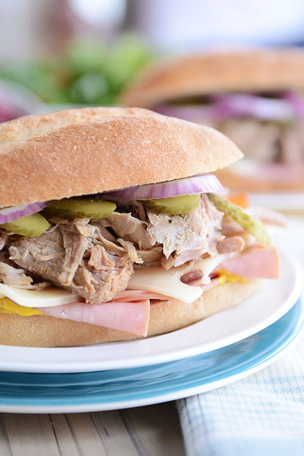 A Cuban sandwich full of pork, cheese, pickles, and onions on a white plate.