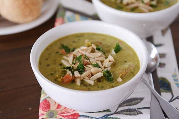 A white bowl of curry soup topped with sliced almonds. 
