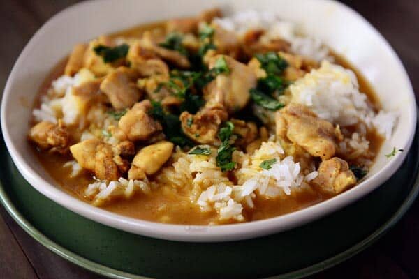 A white bowl of cooked white rice topped with chicken curry and sauce.