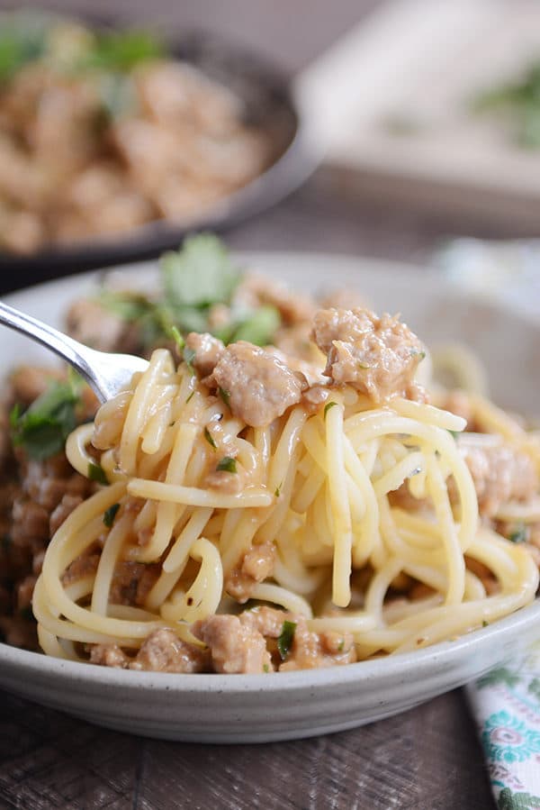 A fork taking a bite of spaghetti noodles and ground beef out of a white bowl.