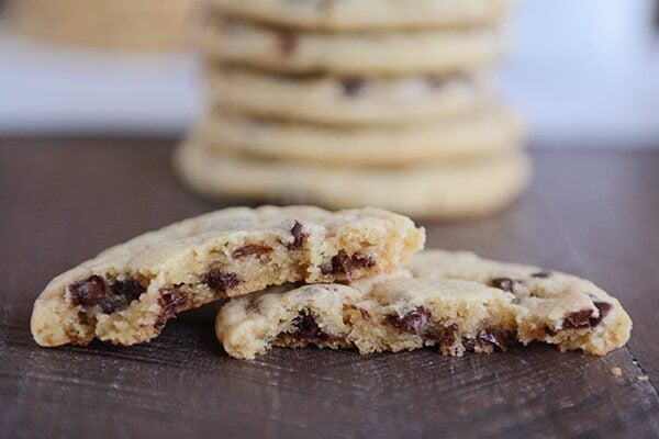 A stack of chocolate chip cookies behind a cookie split in half.