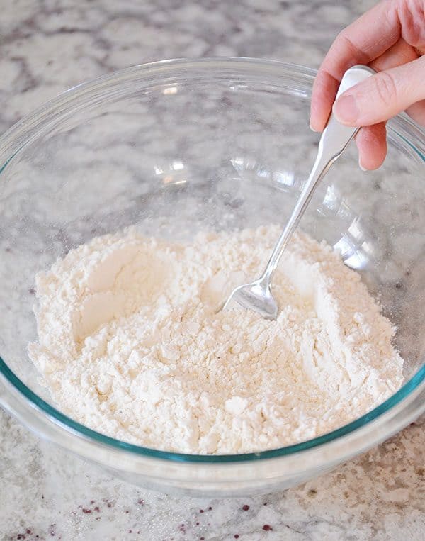 A fork stirring flour in a glass bowl.