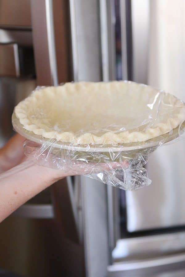 A saran wrap covered pie crust getting held.